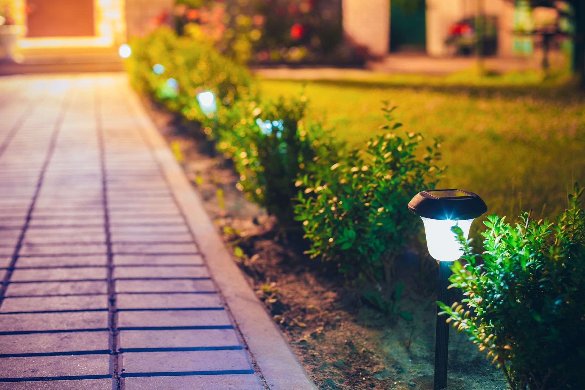 A row of solar powered lights on a sidewalk in front of a house at night.