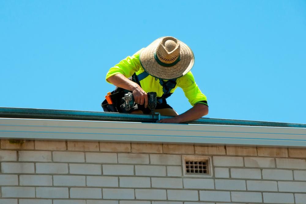 A Man Wearing a Straw Hat Is Working on The Gutter — Bradley Roofing in Tuncurry, NSW