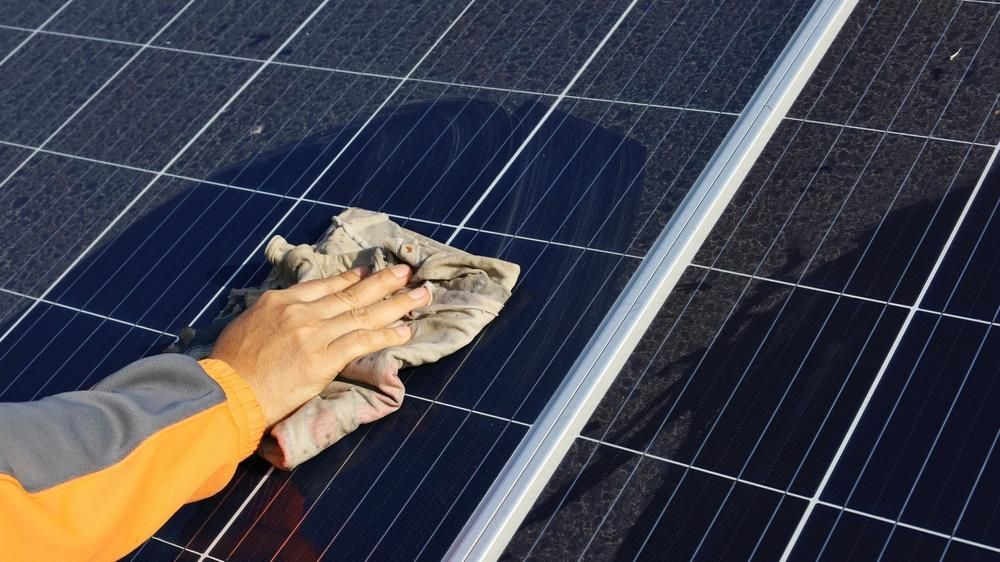 A Person Is Cleaning a Solar Panel with A Cloth — Bradley Roofing in Tuncurry, NSW