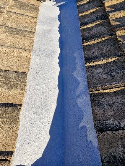 White and blue roofing material being installed in a channel between roof tiles. — Bradley Roofing in Tuncurry, NSW
