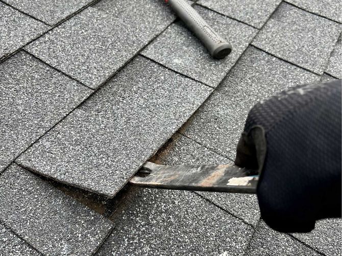 A person is using a hammer to remove shingles from a roof.