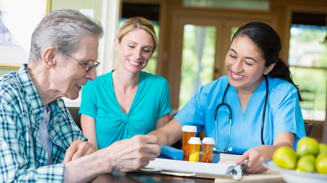An elderly man is sitting at a table with a nurse and a doctor.