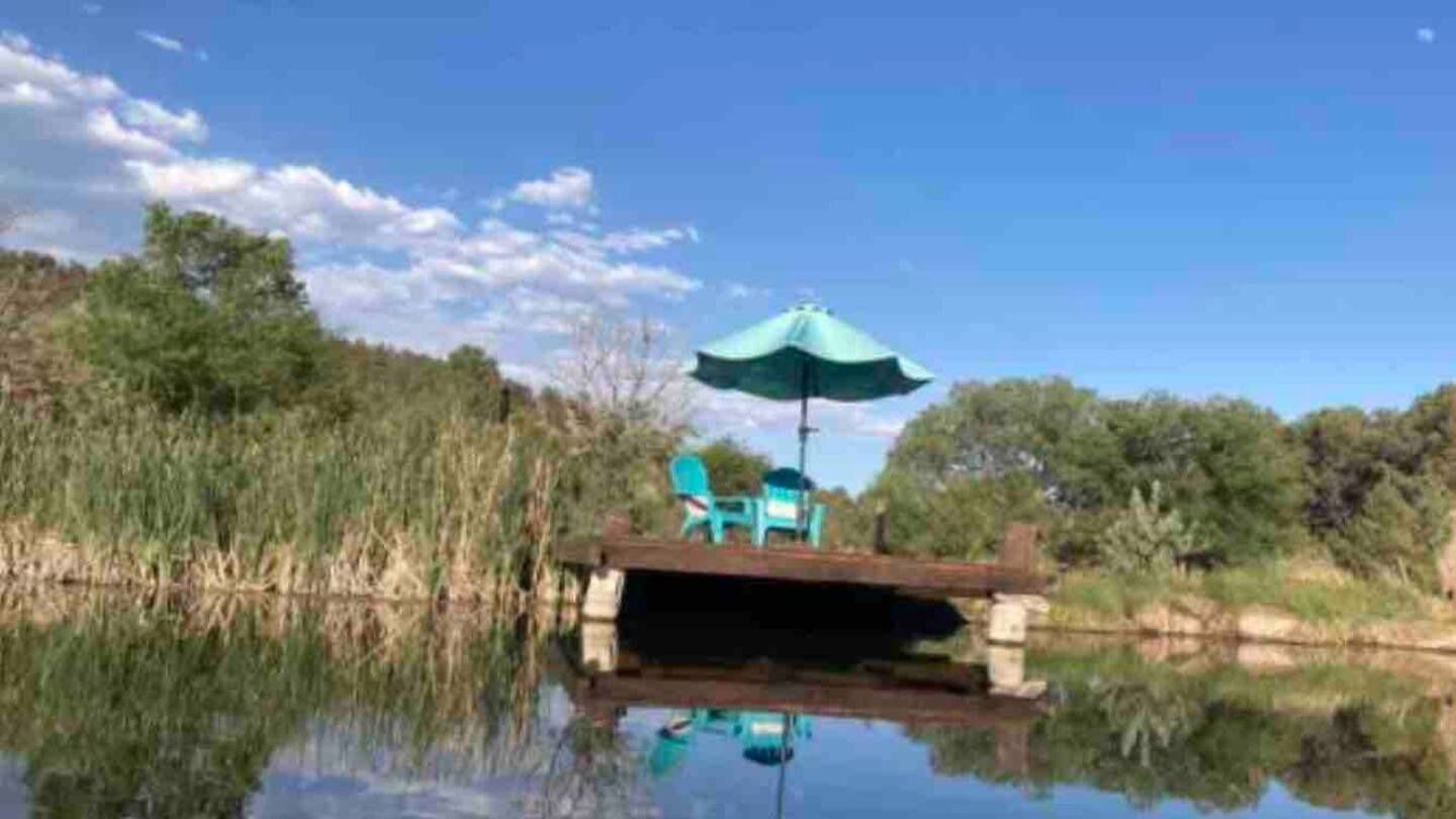 Dock on a calm lake with turquoise chairs, umbrella, and clear blue sky.