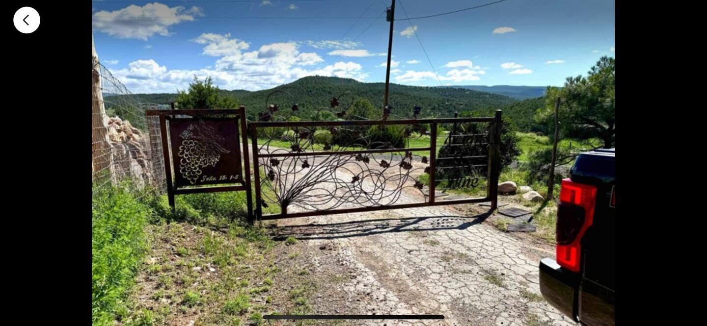 A decorative metal gate opens onto a gravel road, with a vista of green hills and blue sky.