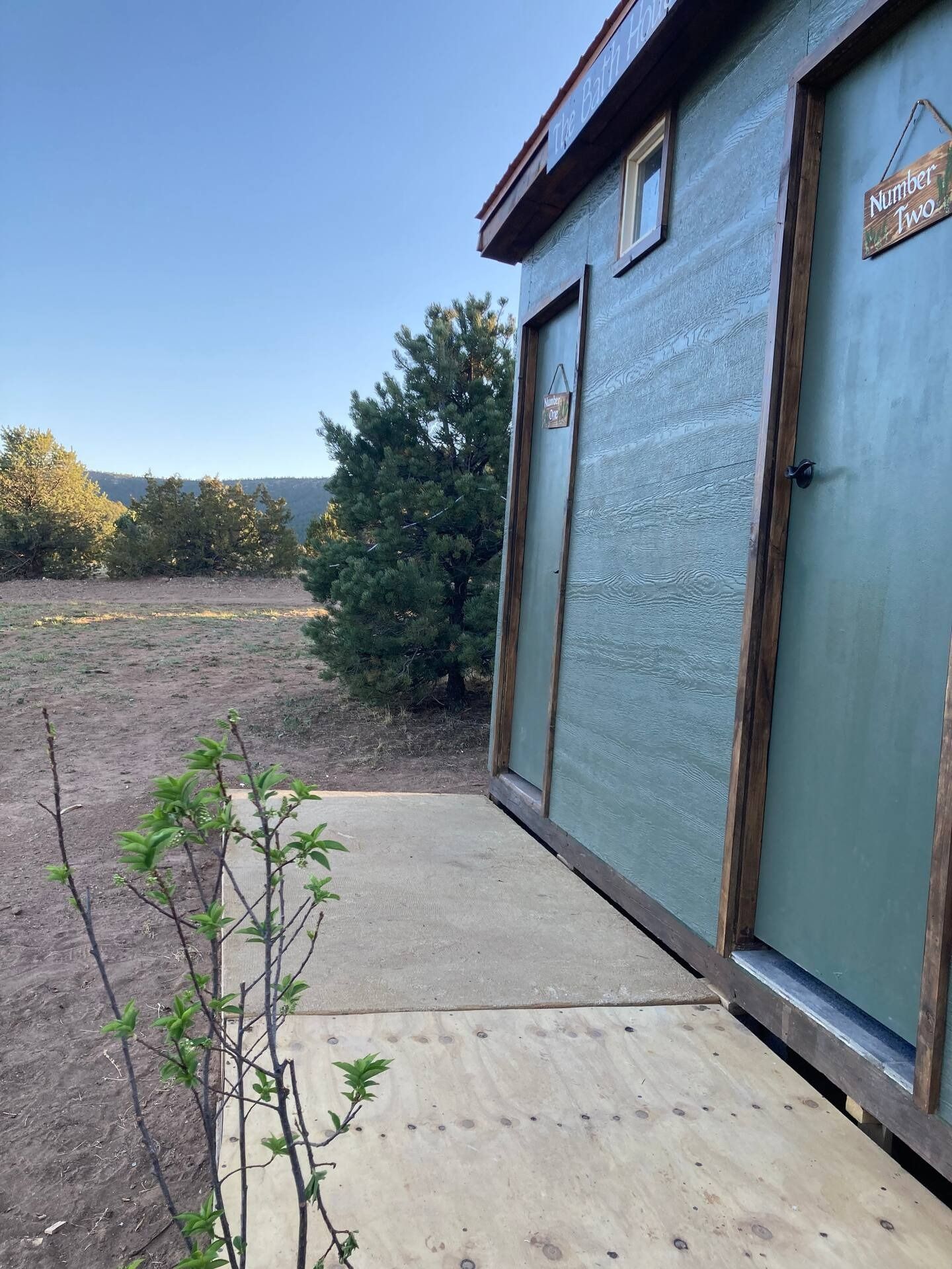 Outdoor restroom building with two doors, surrounded by dry landscape and trees.
