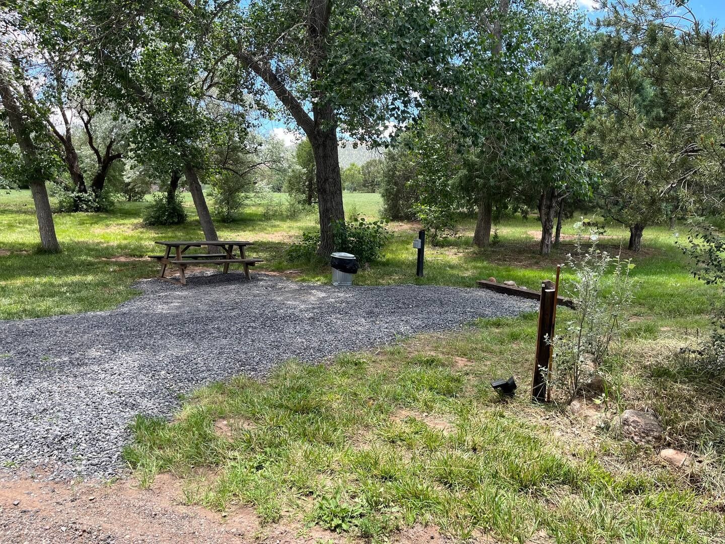 Gravel campsite with picnic table, trees, and trash can.