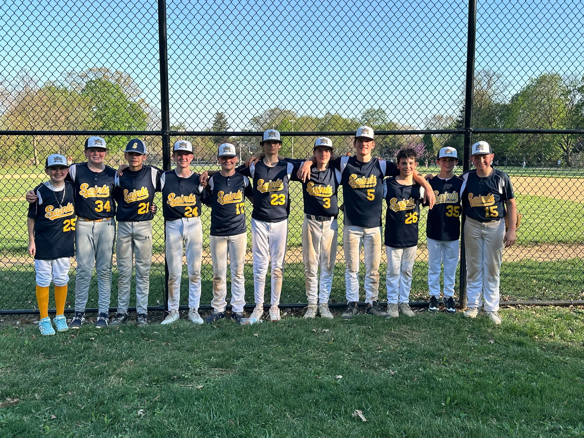Youth baseball team in navy jerseys and white pants posing together on a field behind a fence.