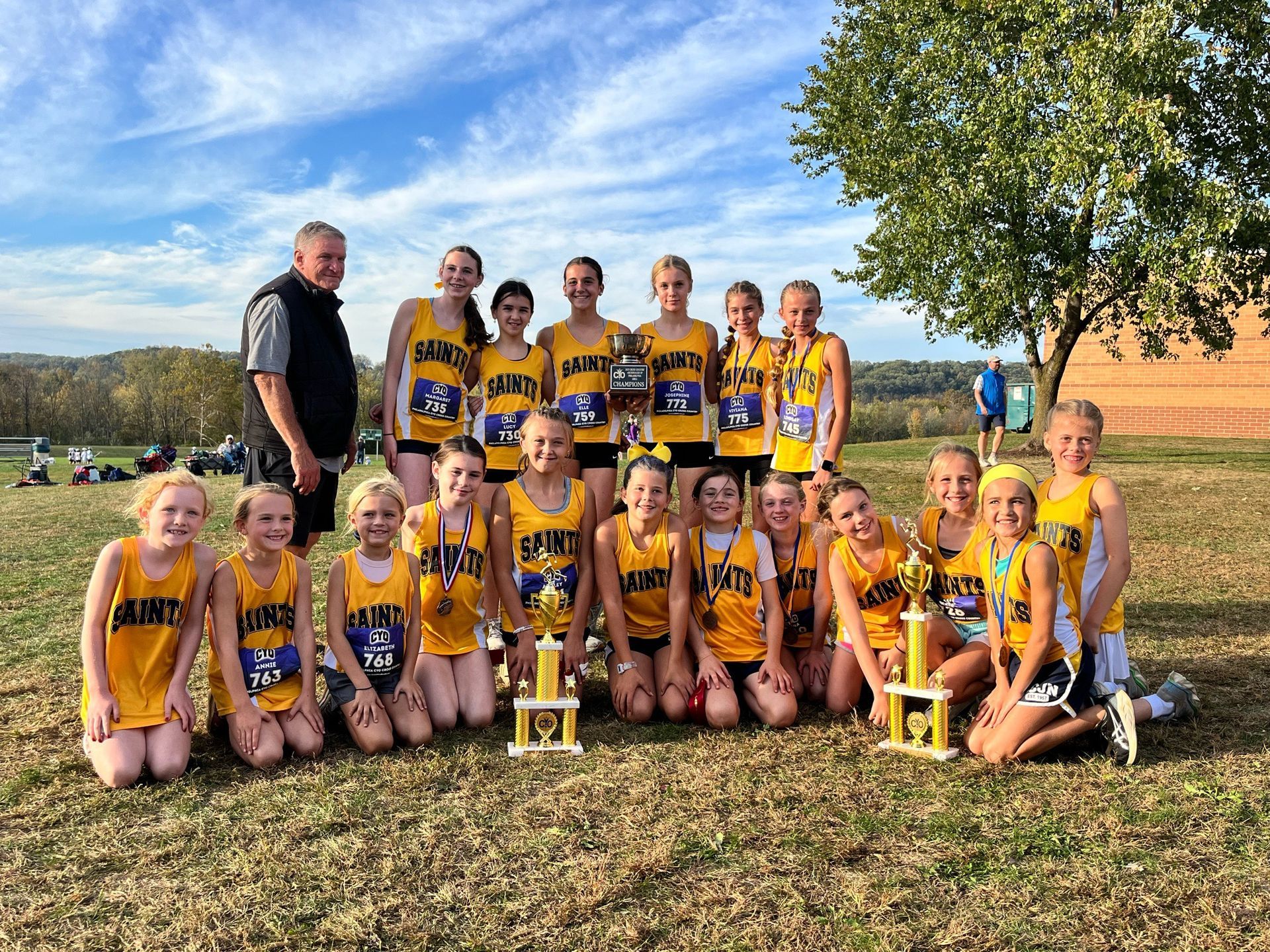 Youth sports team posing outdoors with trophies in yellow-and-purple uniforms