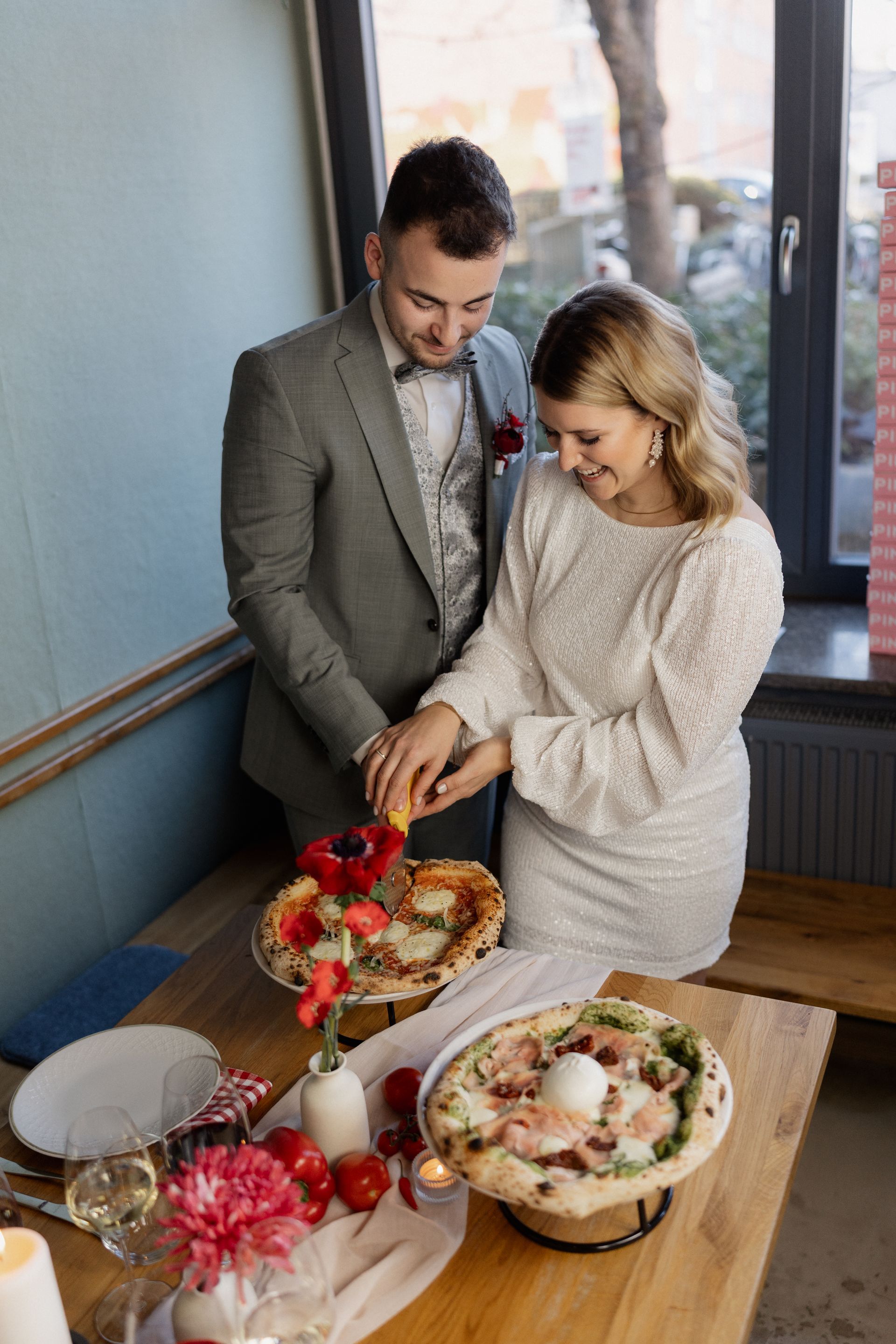 A bride and groom are cutting a pizza at their wedding reception.