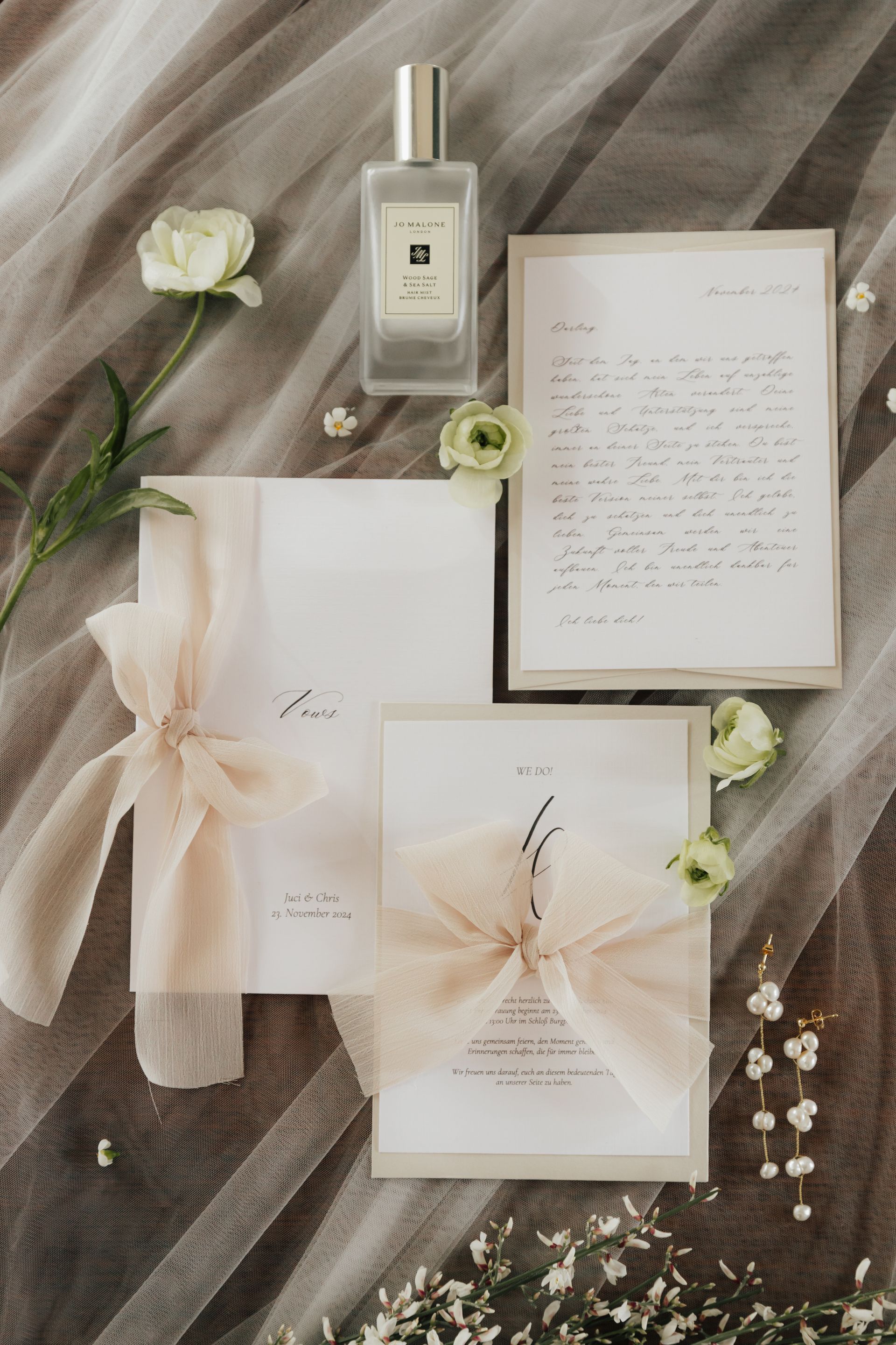 A wedding invitation and a bottle of perfume are sitting on a bed.