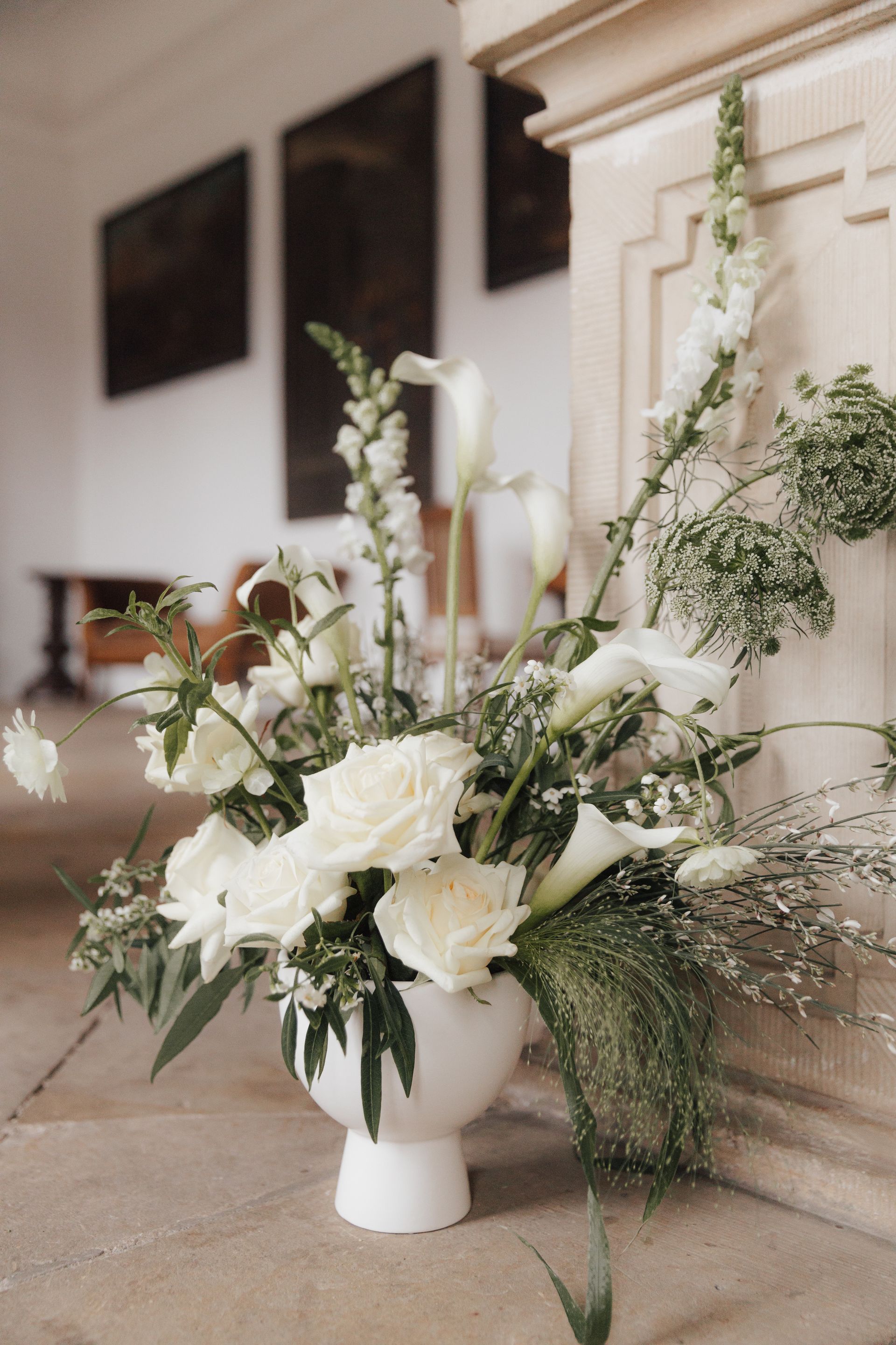 A vase filled with white flowers is sitting on the floor in a church.