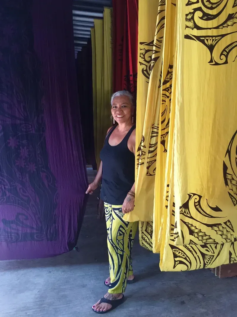 A woman in a black tank top and yellow pants is standing in front of yellow curtains.