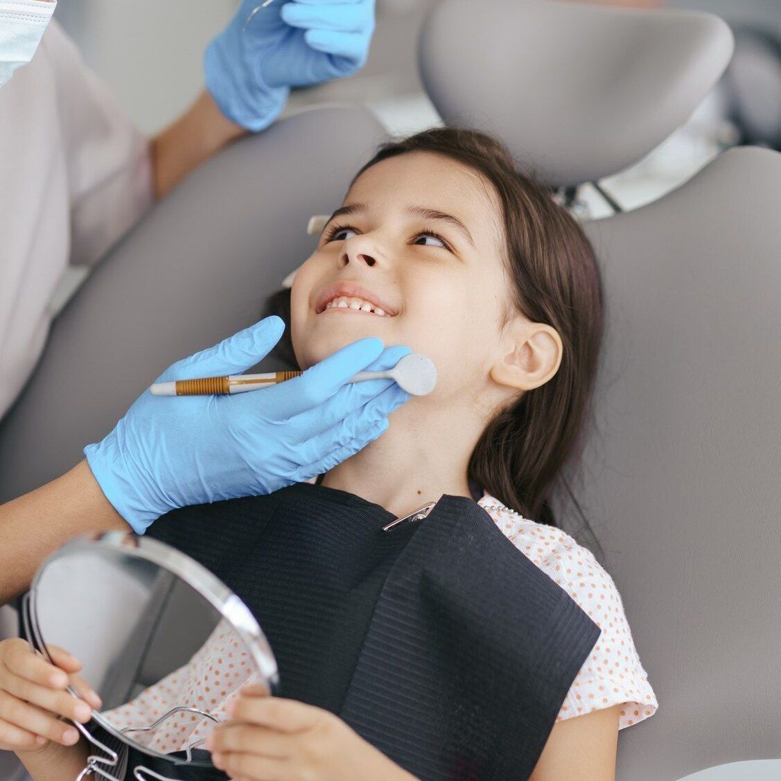 A little girl is sitting in a dental chair getting her teeth examined by a dentist.