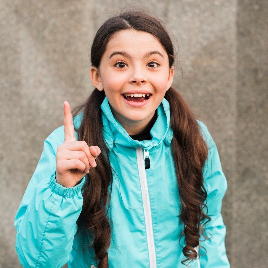 A young girl in a blue jacket is giving a thumbs up sign.