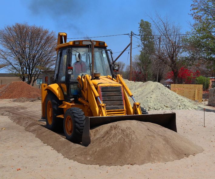 Yellow backhoe loader pushing sand in a construction site under a clear blue sky