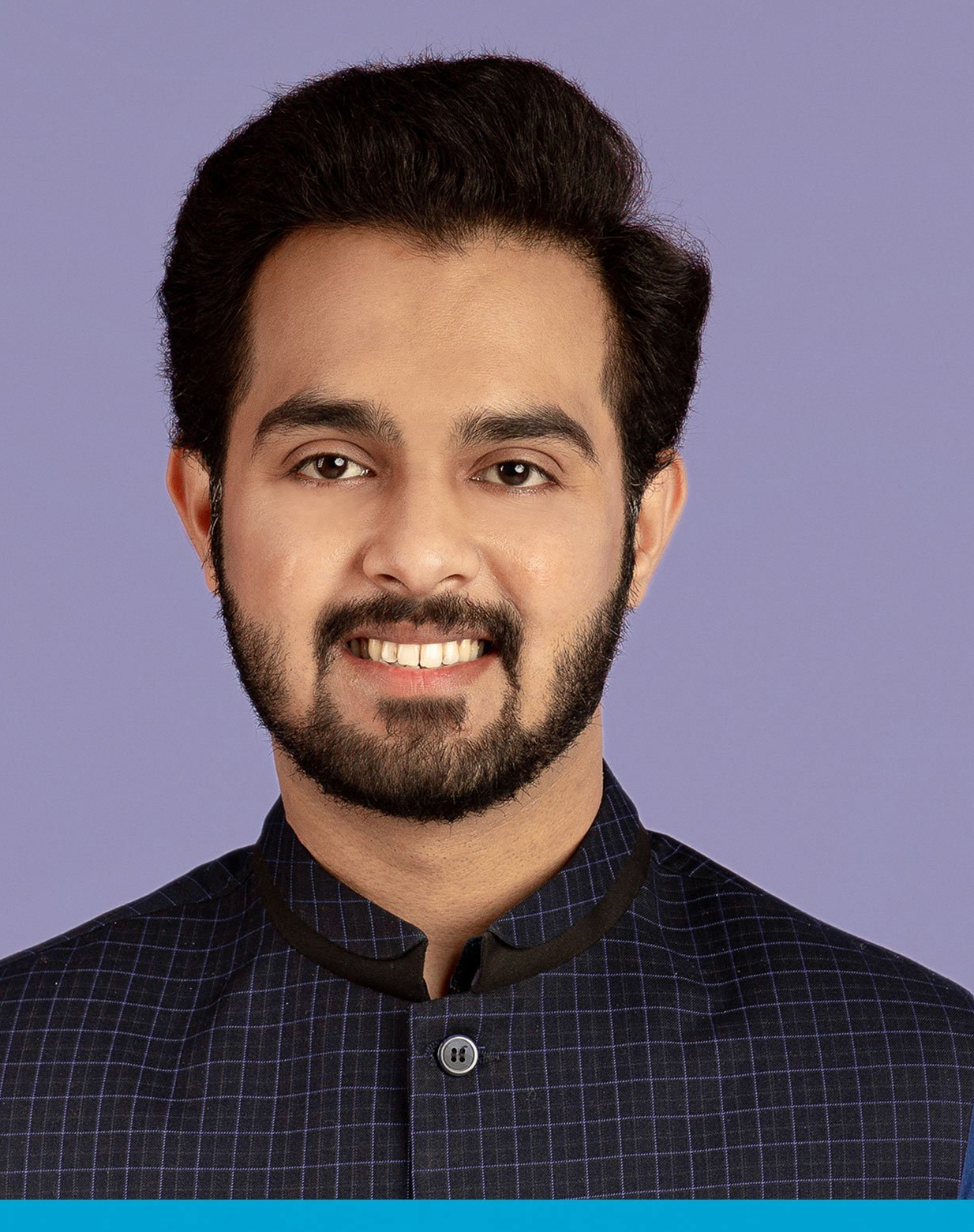 Man with dark hair and beard, smiling. Wearing a dark jacket with a blue background.