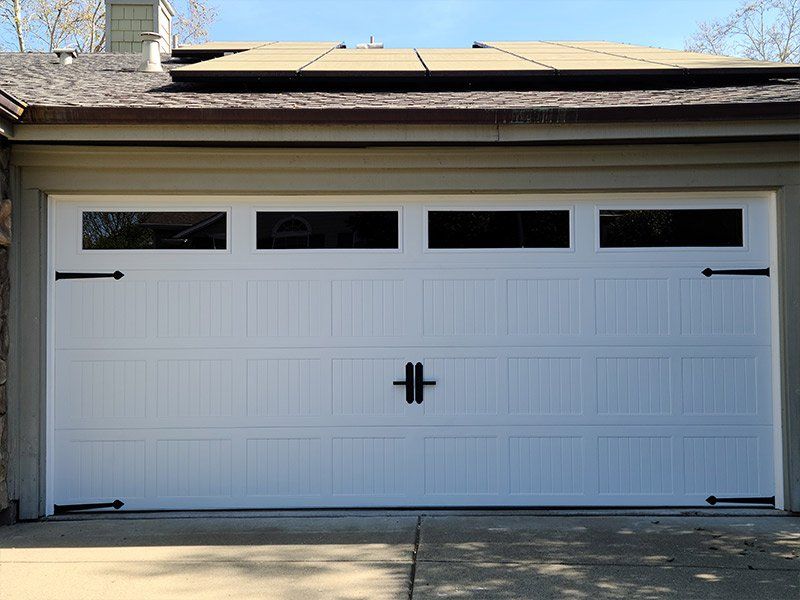A white garage door with black handles is sitting in front of a house.