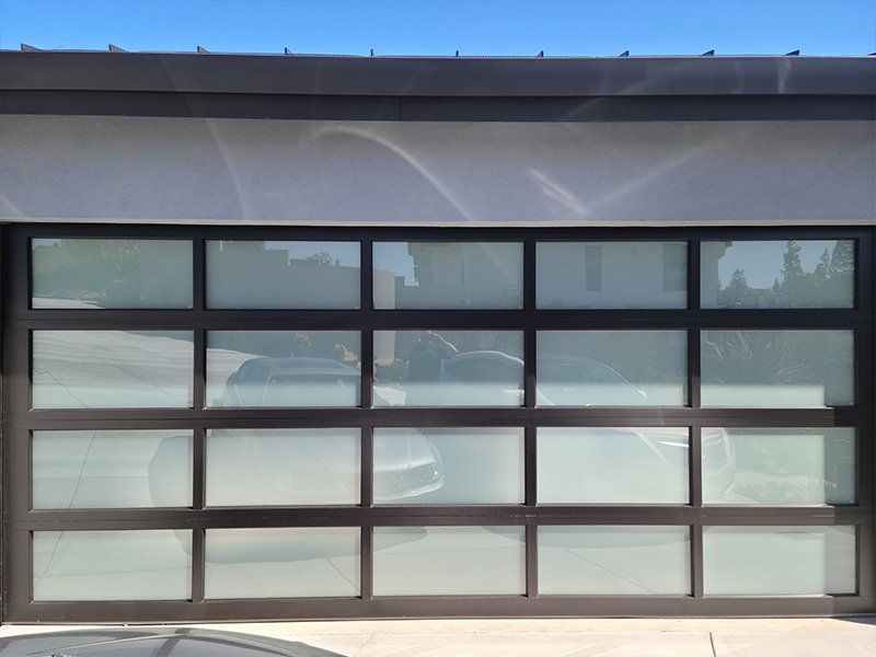 A car is parked in front of a garage door with a lot of windows.