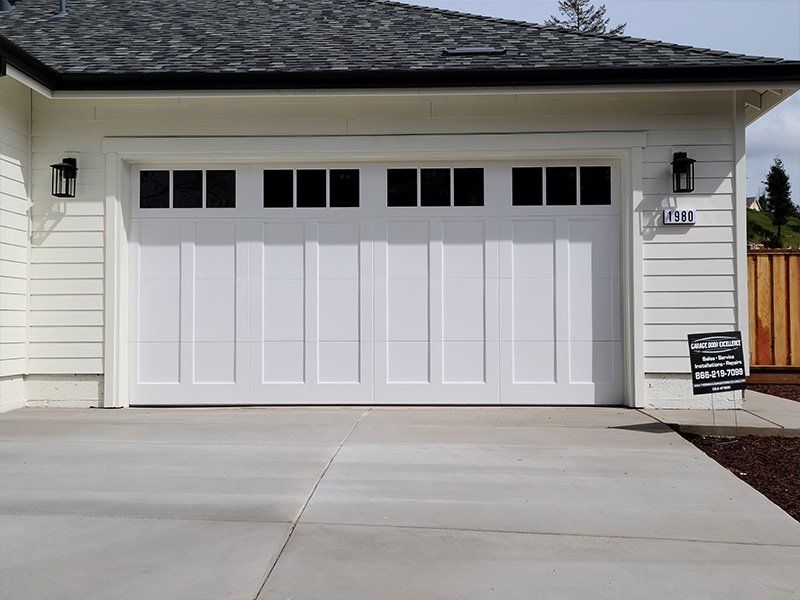 A white garage door is sitting in front of a white house.
