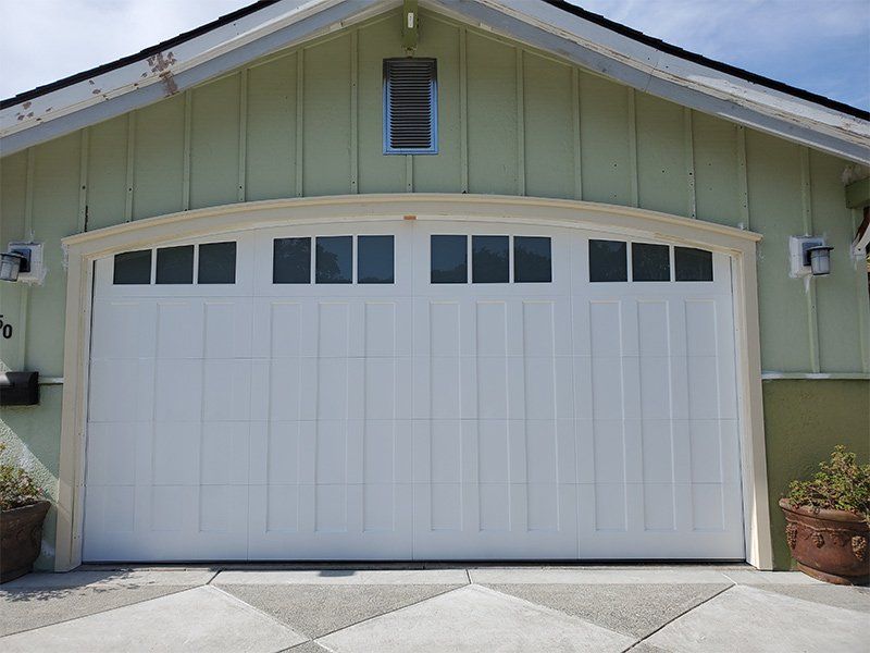 A white garage door is sitting in front of a green house.