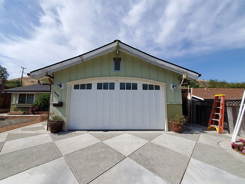 A green house with a white garage door and a ladder in front of it.