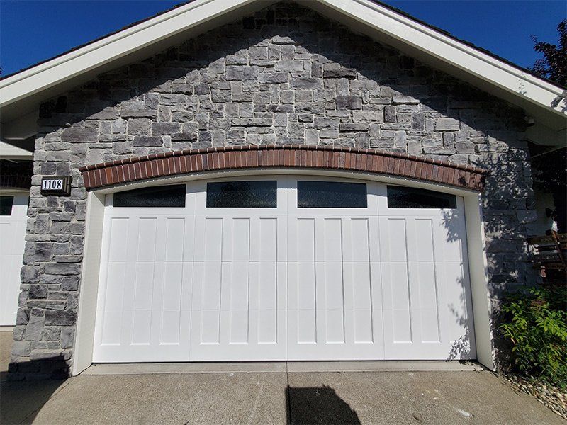 A white garage door is in front of a stone house