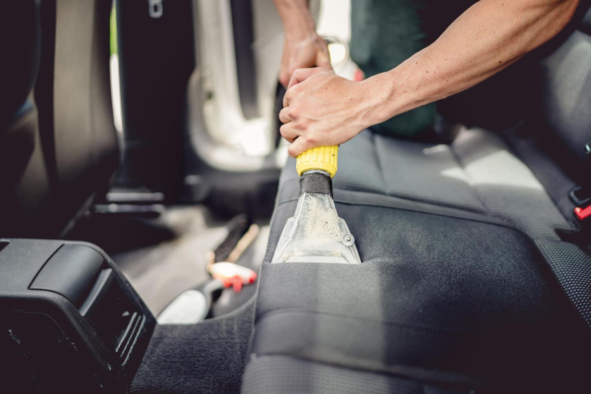 A man is cleaning the back seat of a car with a vacuum cleaner.