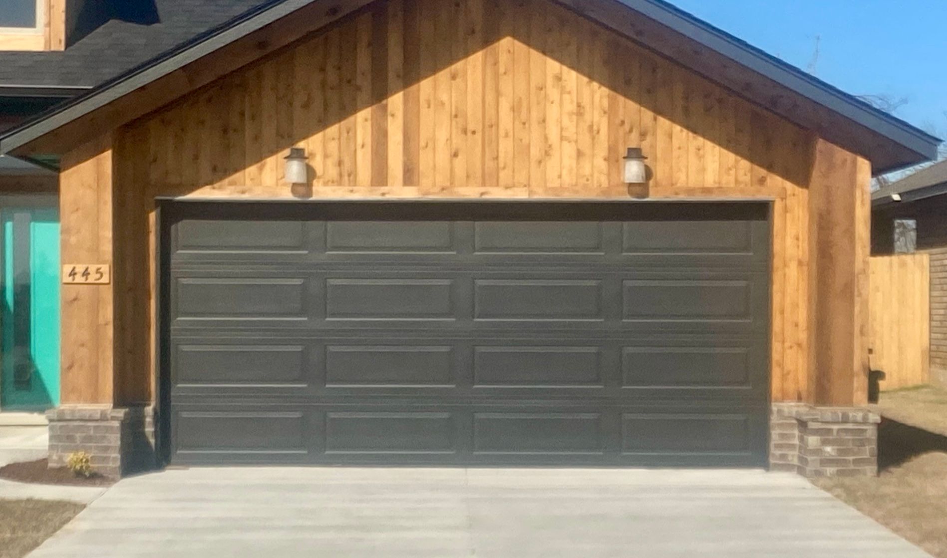 Modern house front with wood siding and a large dark gray garage door above a concrete driveway
