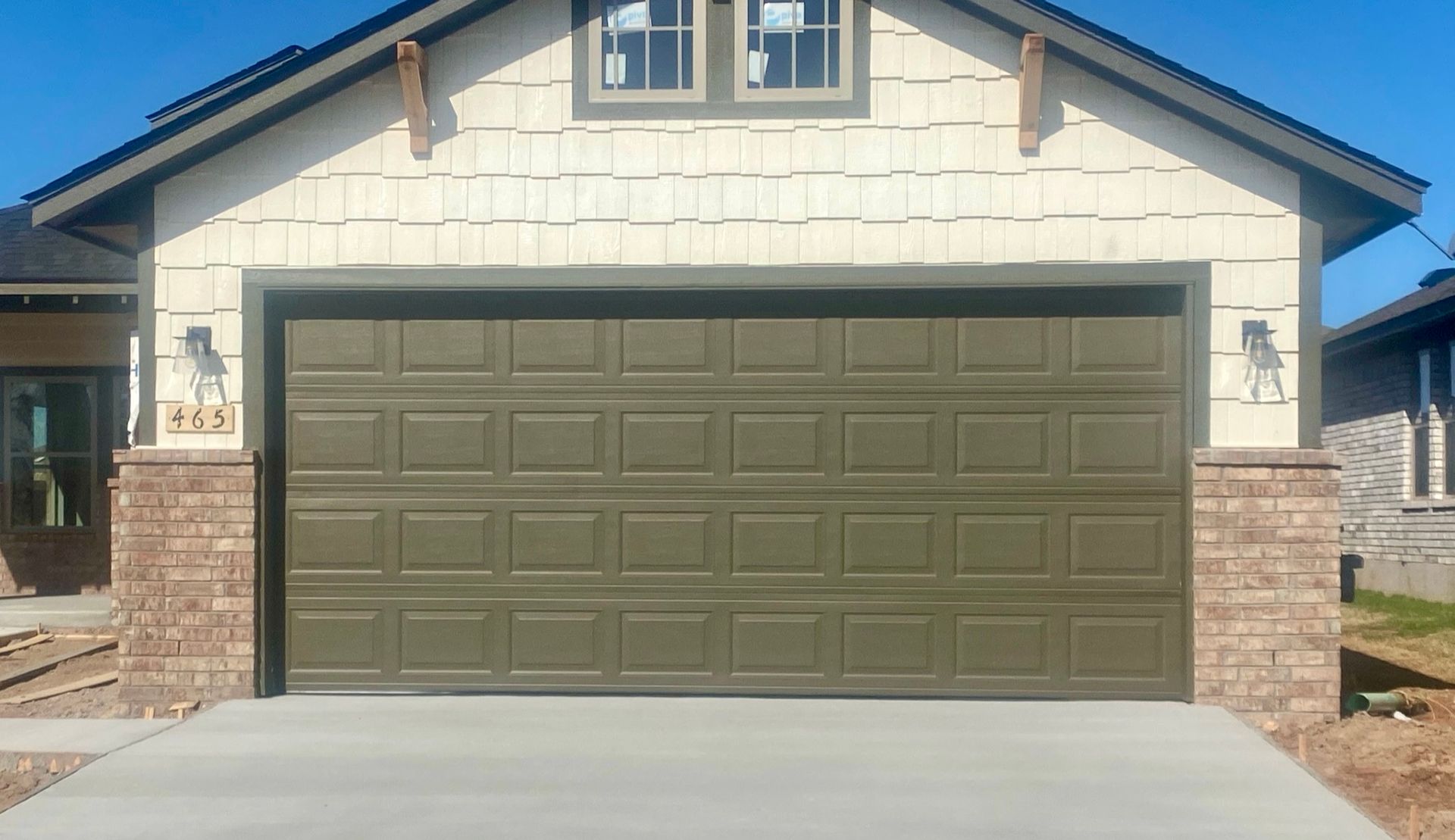 Front view of a house with a closed olive-green garage door and stone columns.
