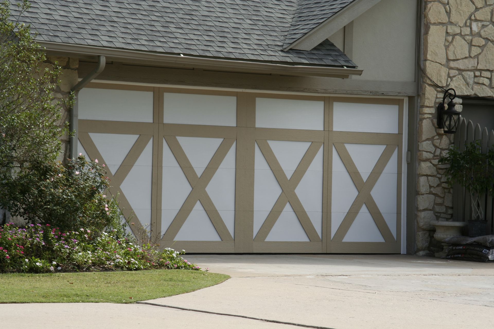 White garage doors with tan X-brace trim on a suburban house beside a driveway and garden