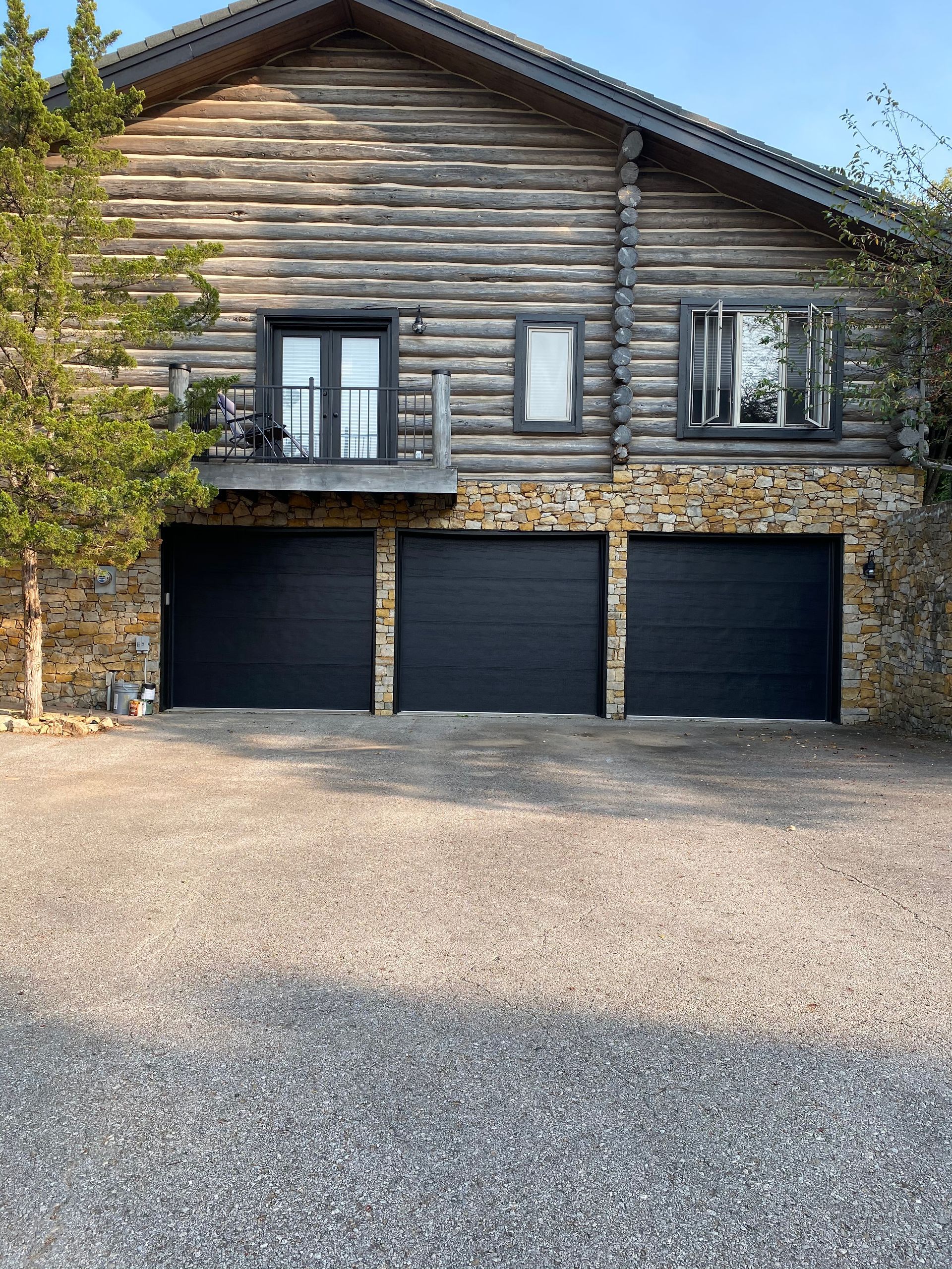 Log cabin-style house with three black garage doors and a gravel driveway in front