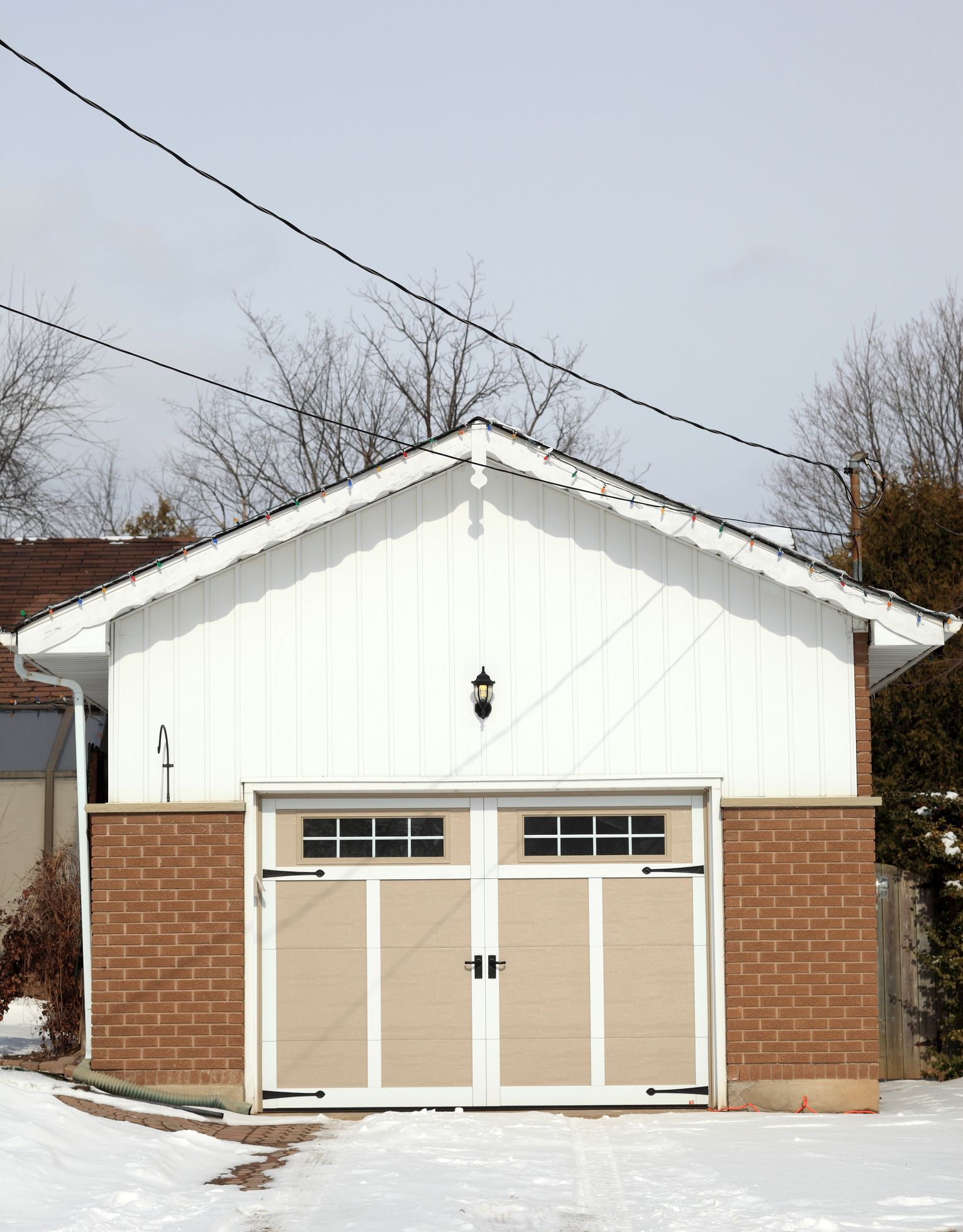 White and brick detached garage with double doors on a snowy residential lot