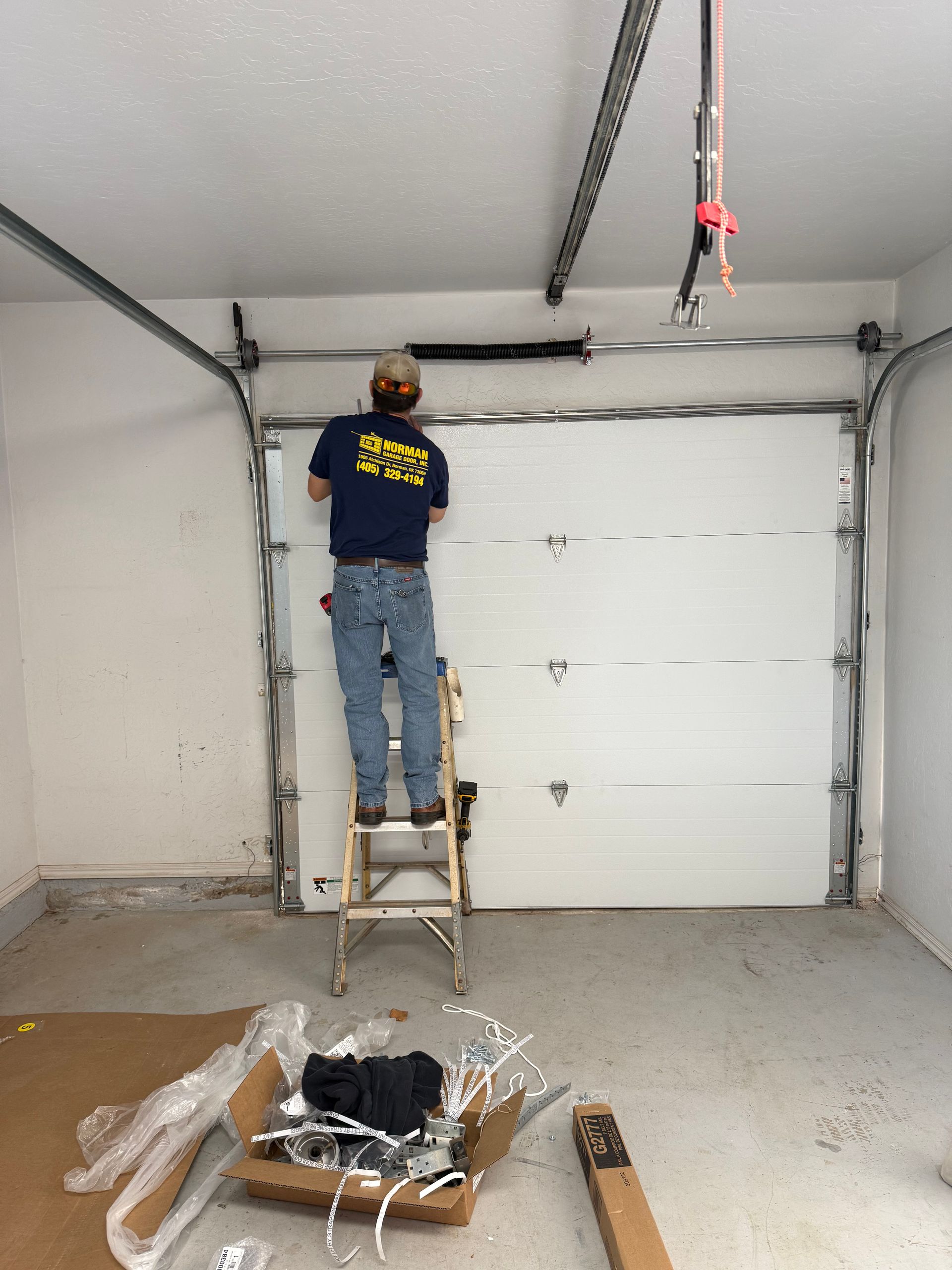 Person on a stepladder installing garage door hardware in a white garage