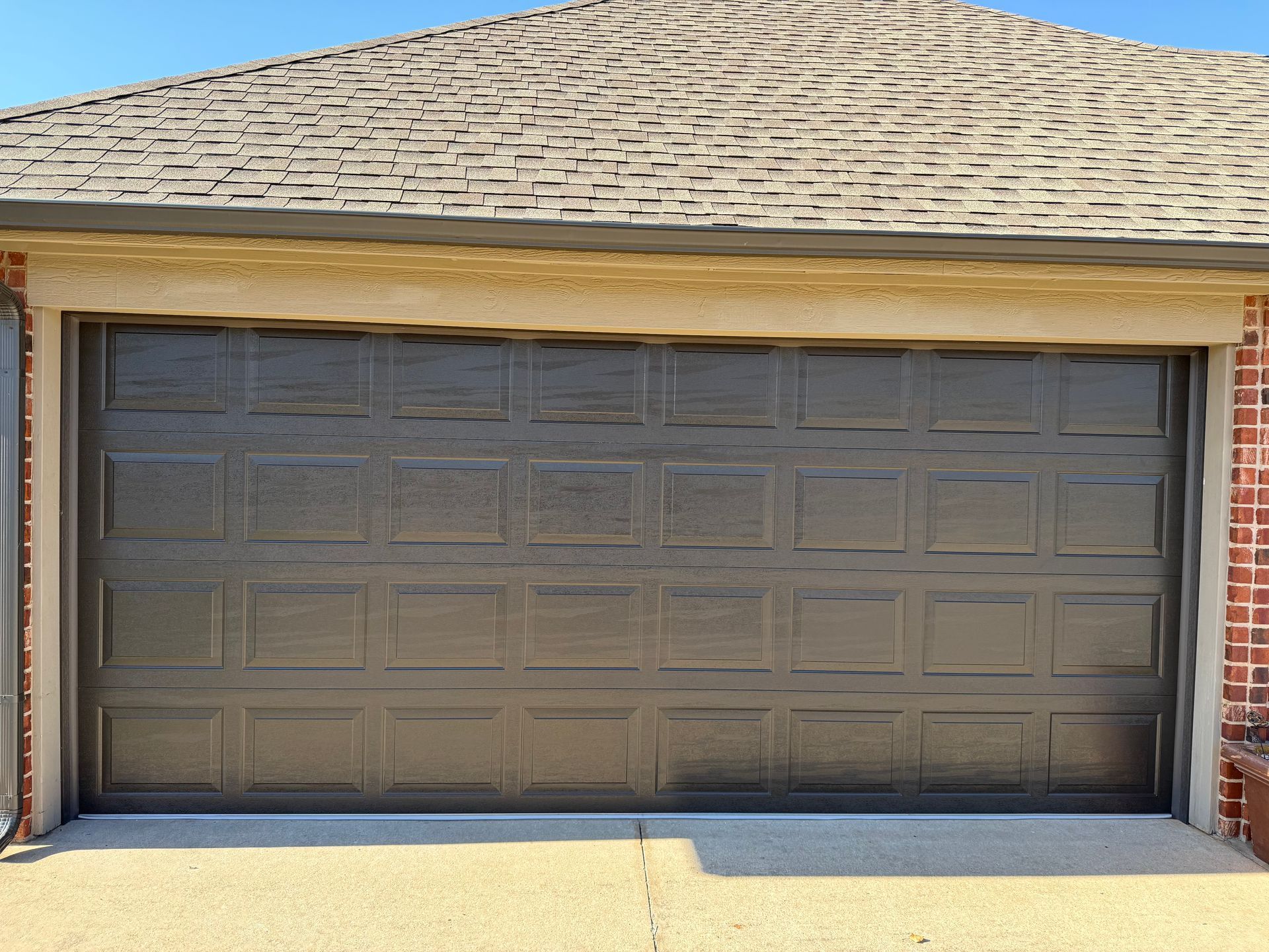 Closed gray double garage door on a brick house under a shingled roof
