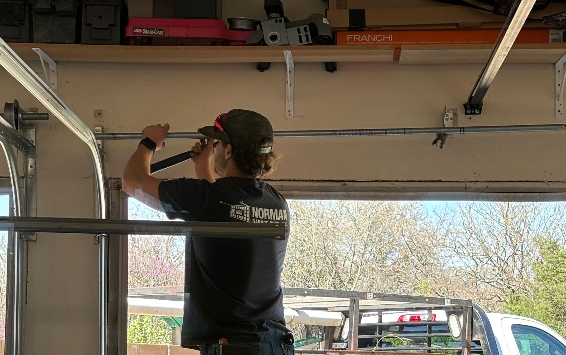 Person in a garage using a hammer to work on the garage door track.