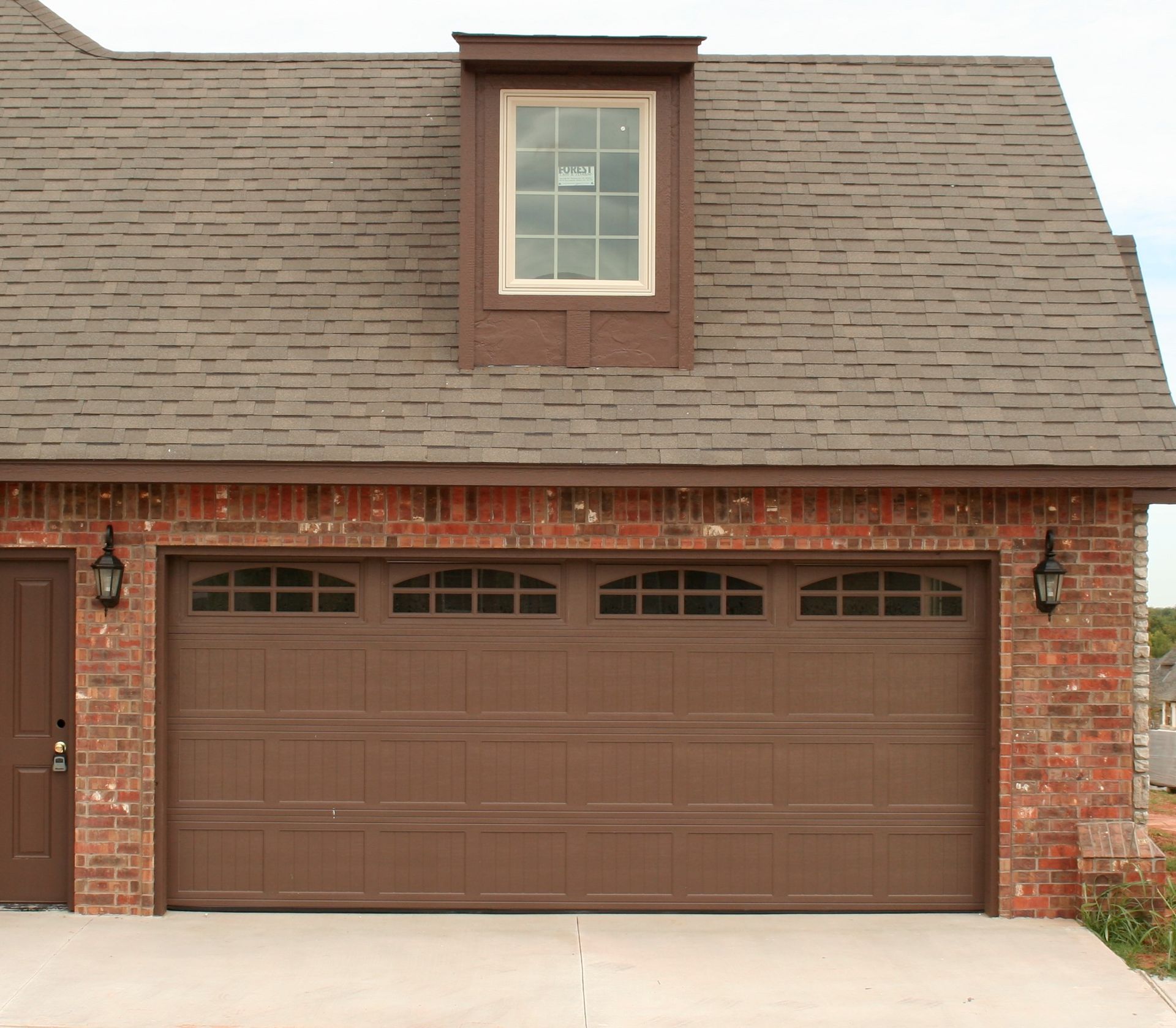 Brick house front with brown garage doors and a small dormer window above
