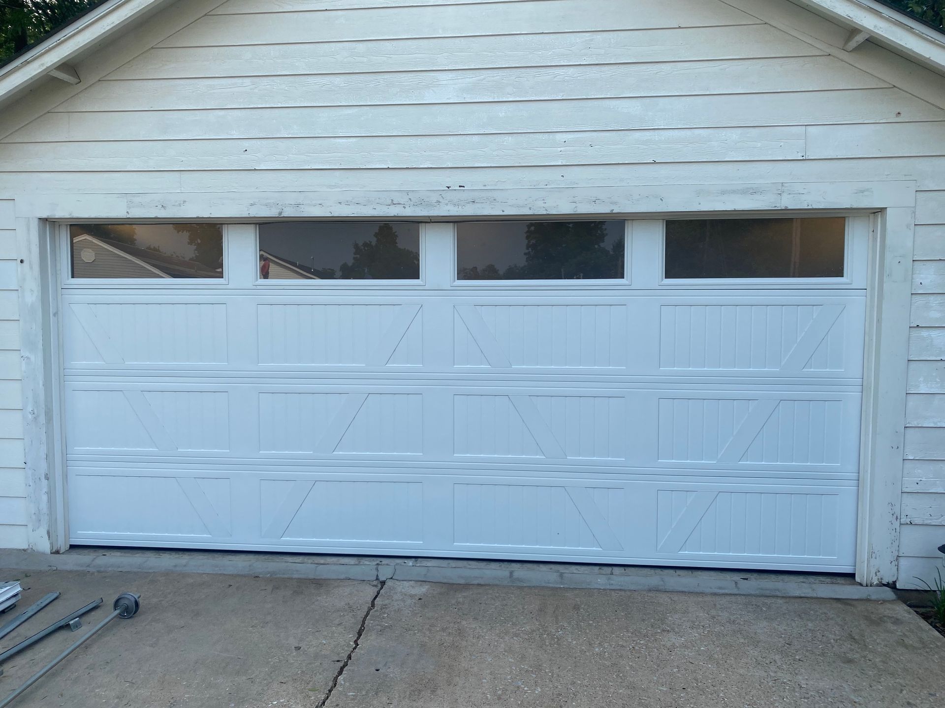 White double garage door with four small windows, slightly dented, on a house exterior.