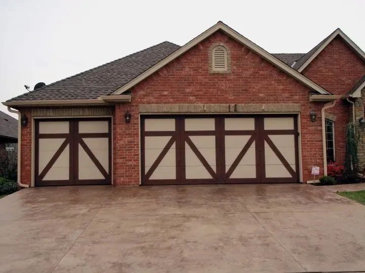 Brick house with three wooden garage doors and a large concrete driveway