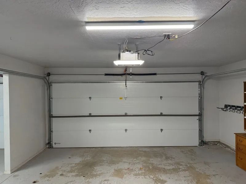Interior view of a two-car garage with white door panels and ceiling-mounted opener.