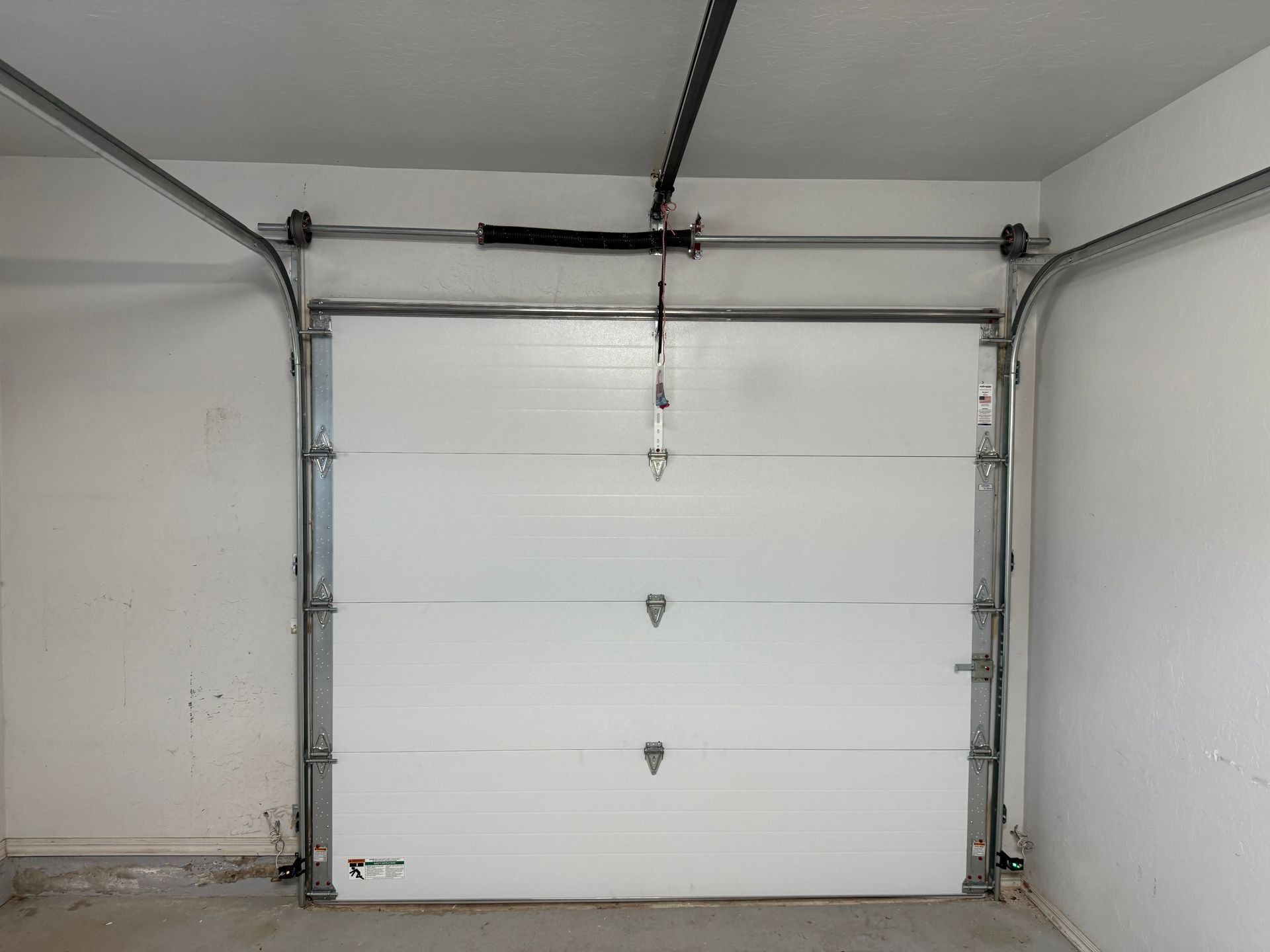White sectional garage door with vertical tracks, rollers, and torsion spring.