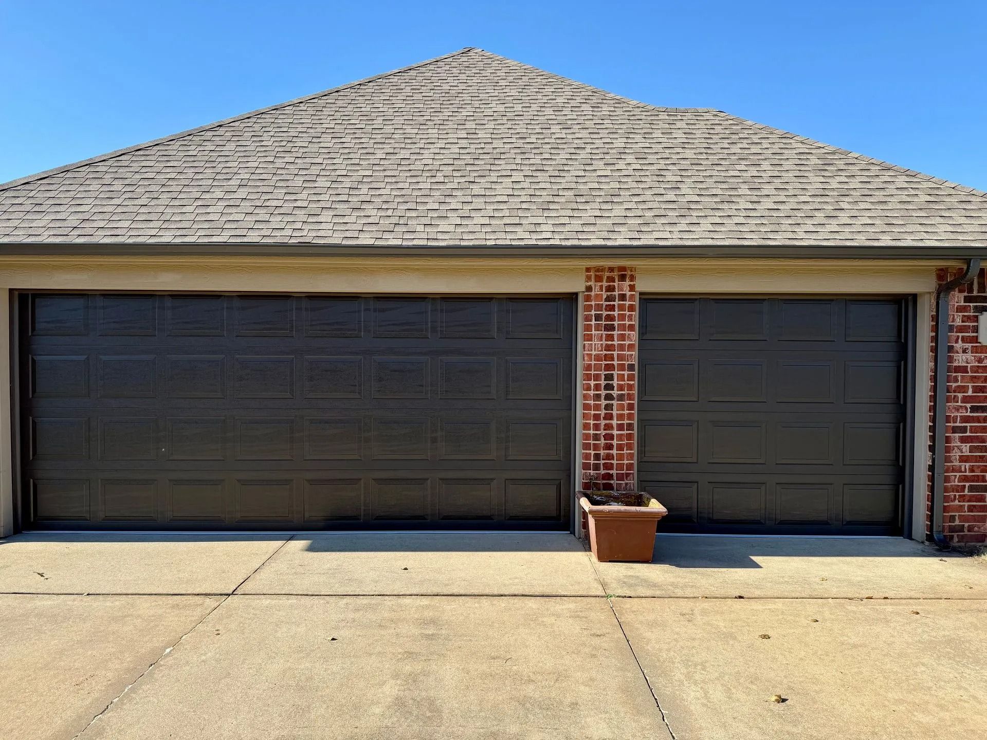 Dark brown two-car garage door on brick home with clear sky.