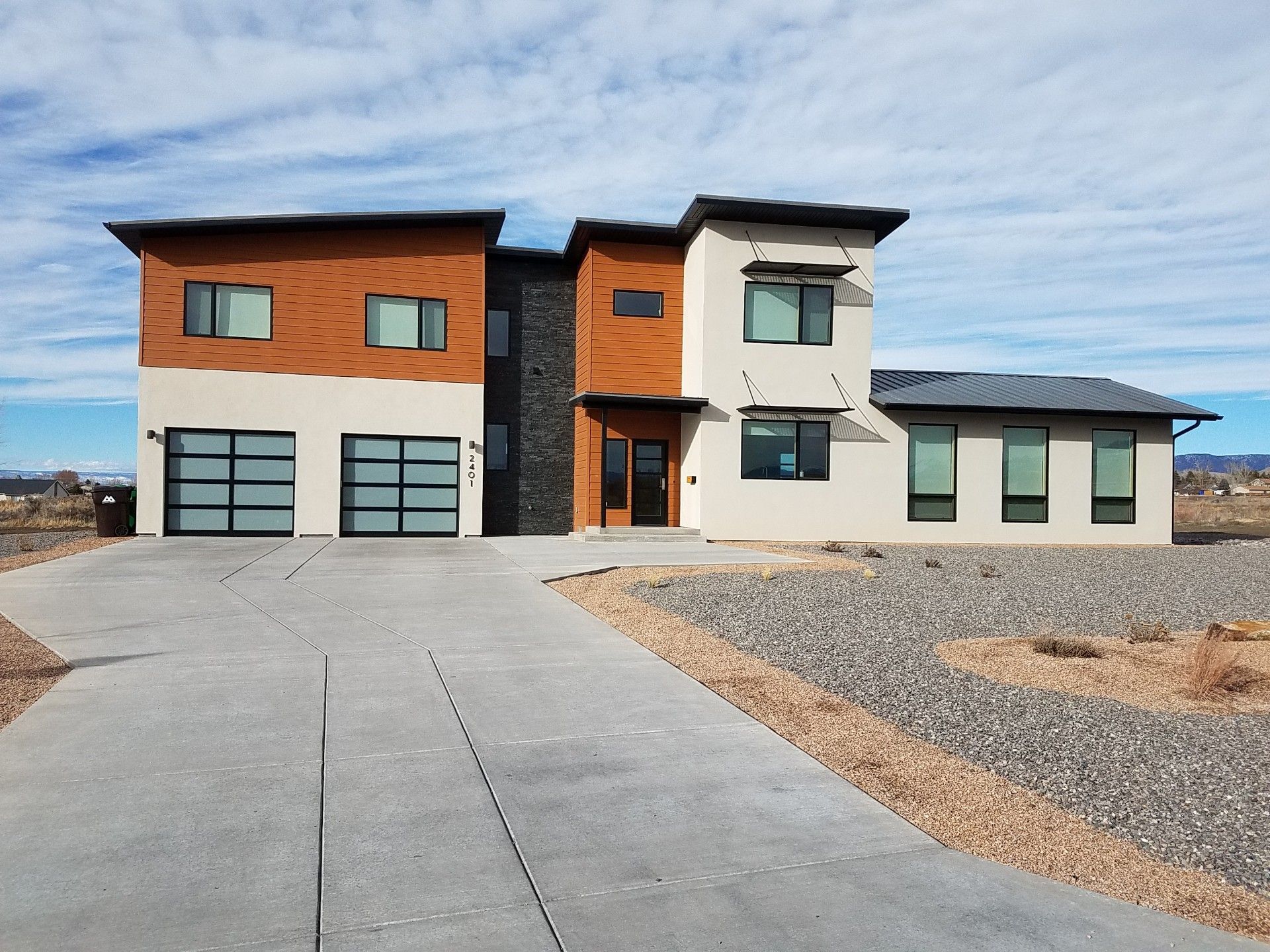 Modern two-story house with wood, white, and stone exterior, front driveway, and desert landscaping