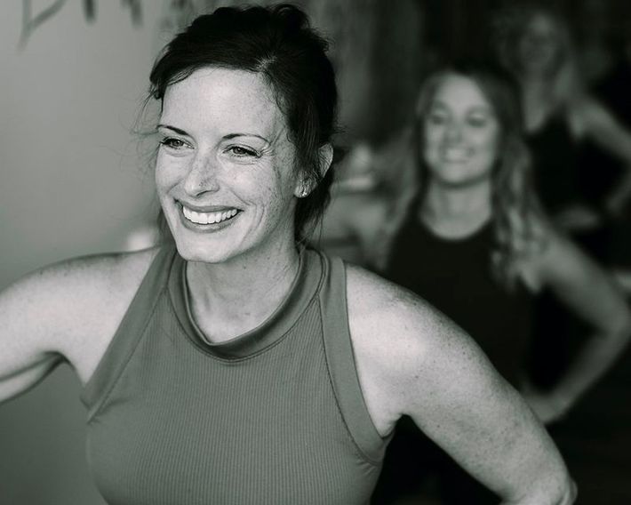 Woman smiles while working out in a studio; another woman smiles in the background.