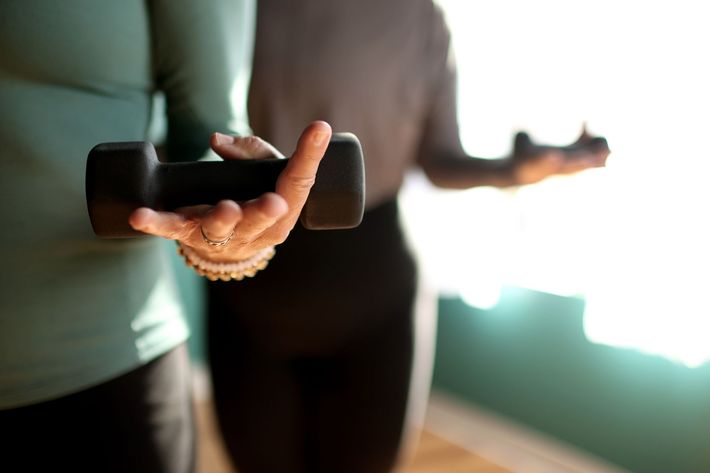 Person holding a black dumbbell, practicing exercise, and standing near a window.