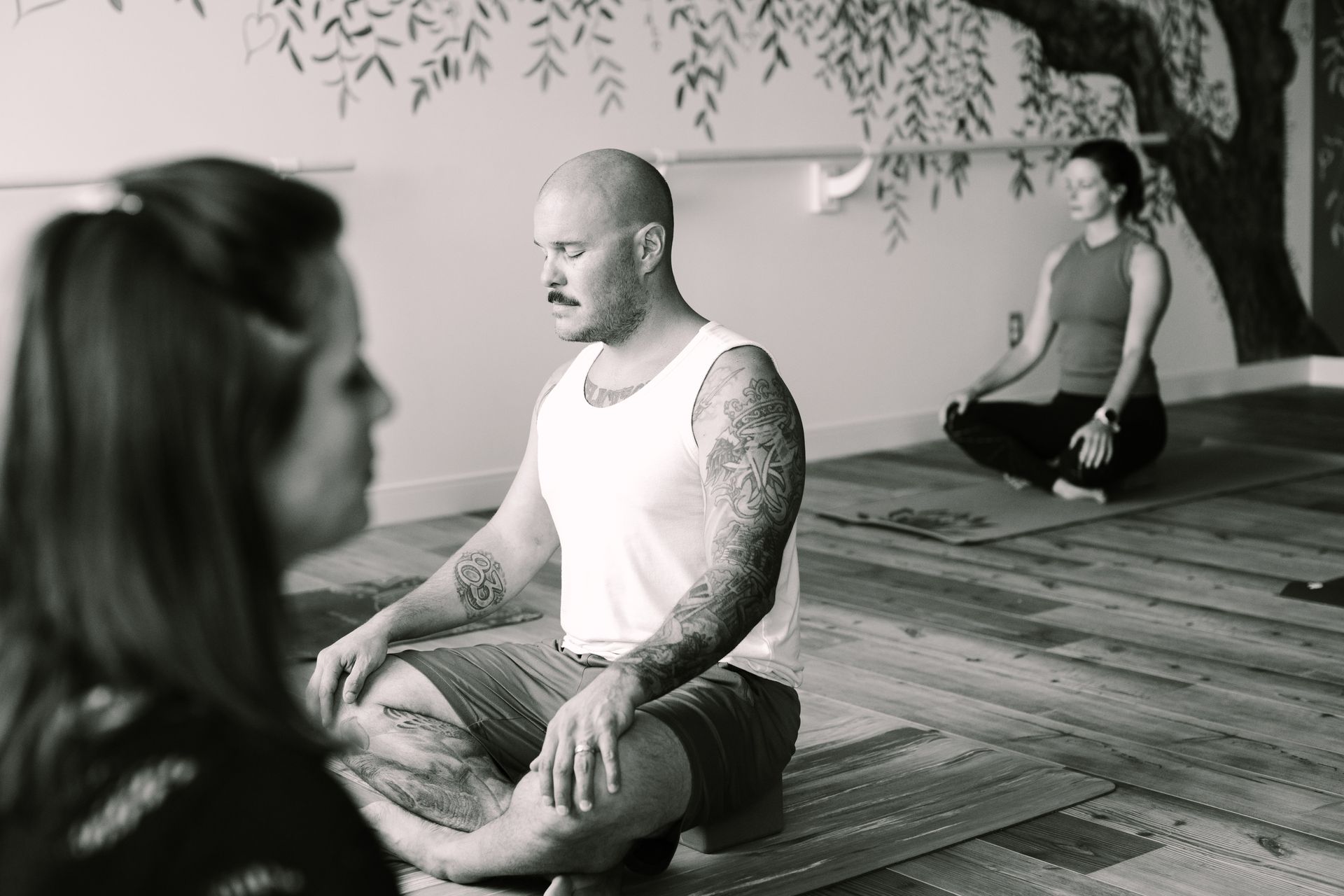 People meditating in a yoga studio with painted tree mural.