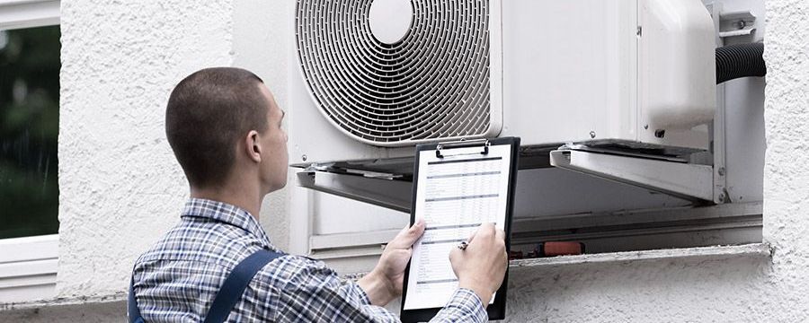 A man is holding a clipboard in front of an air conditioner.
