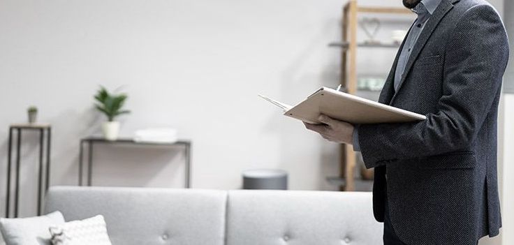 A man in a suit is holding a clipboard in a living room.