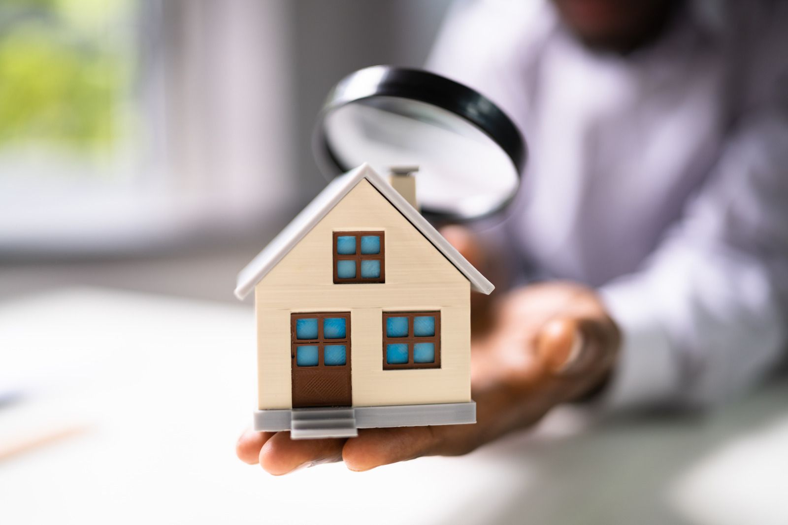 A person is holding a model house with a magnifying glass.