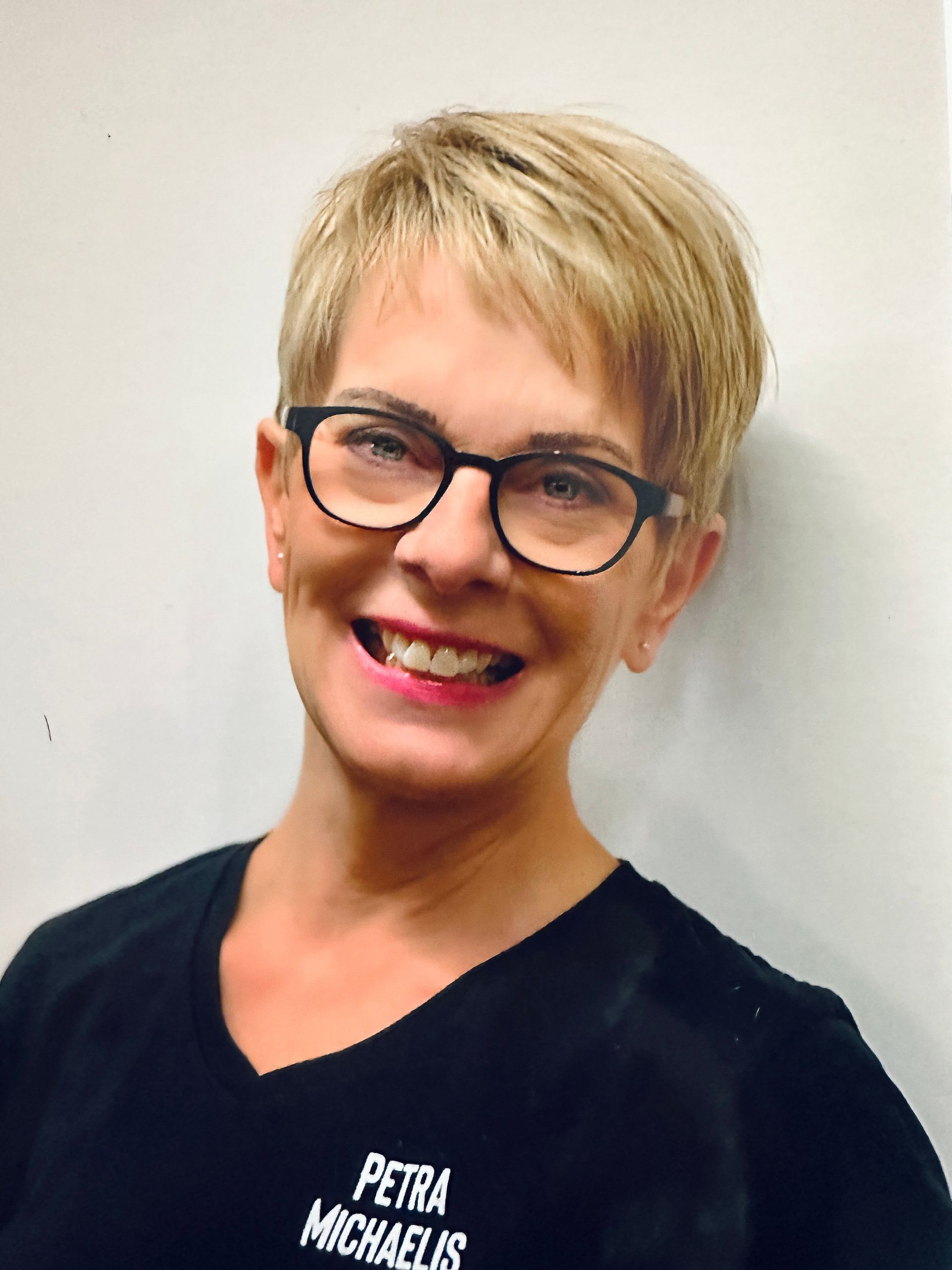 Eine Frau mit kurzen blonden Haaren und Brille lächelt. Sie trägt ein schwarzes Oberteil mit dem Namen „Petra Michaelis“.