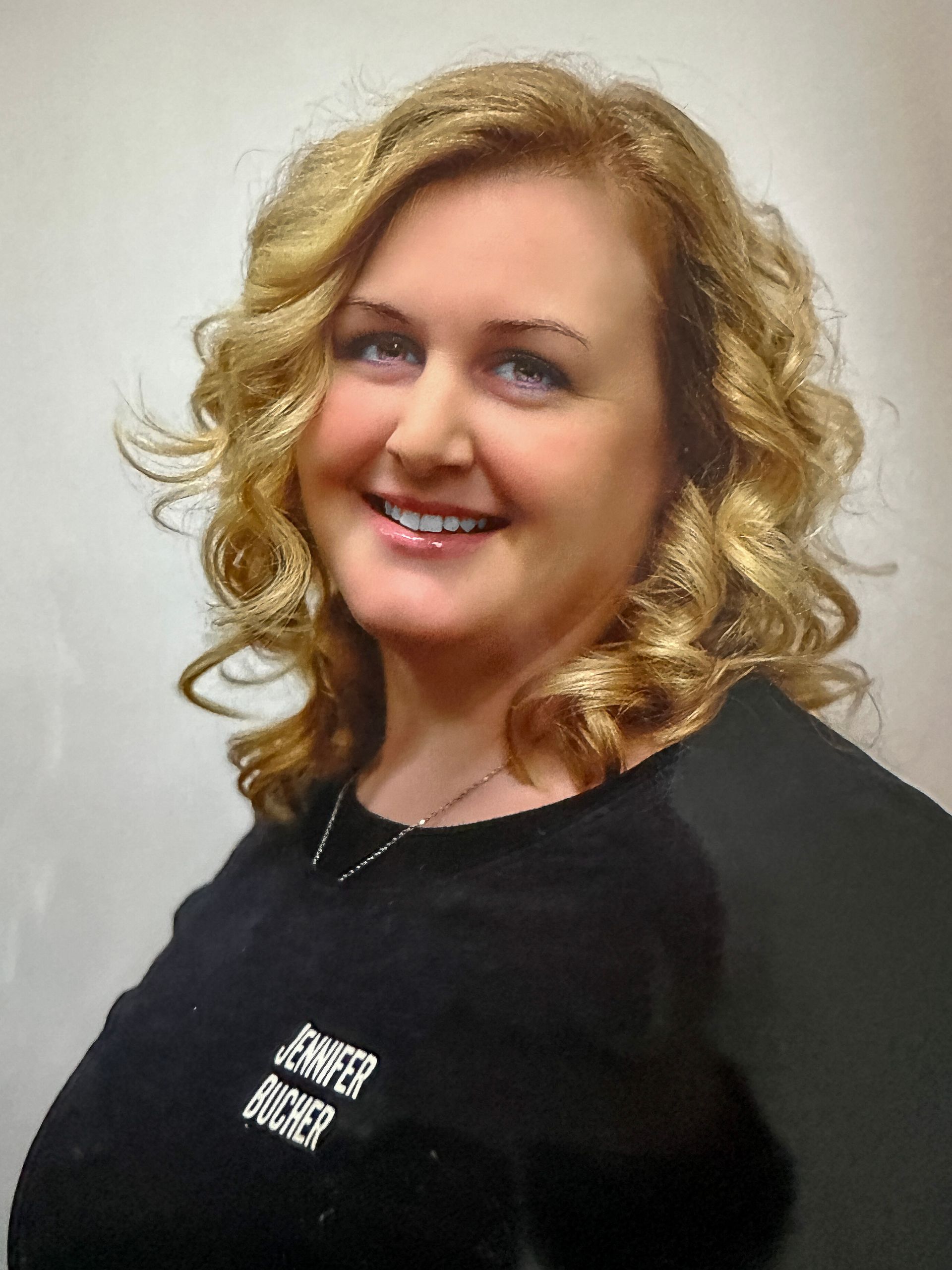 Frau mit lockigem blonden Haar lächelt und trägt ein schwarzes Hemd.